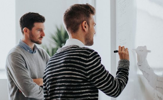 business results man drawing on whiteboard next to other man