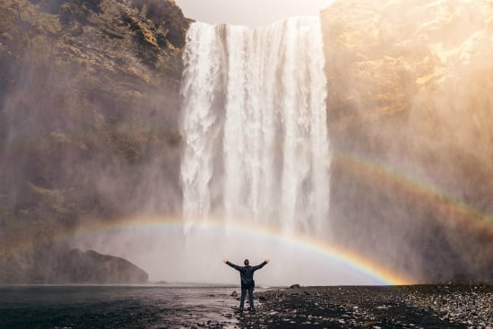 man thinking positive in front of a waterfall and rainbow
